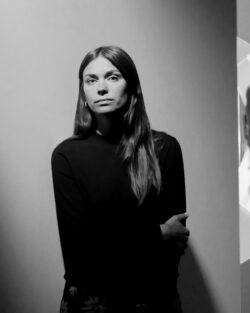 A woman with one arm draped over the other looks into the camera for a portrait.