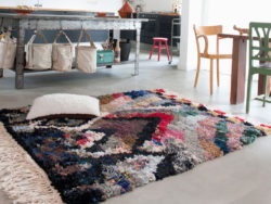A colourful carpet lies on a concrete floor in a kitchen.