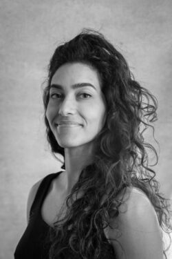 A woman with curly hair smiles radiantly at the camera, showing her cheerful expression.
