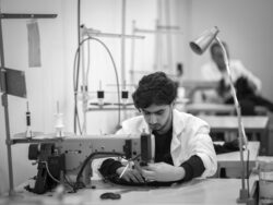 A man sits behind a sewing machine sewing