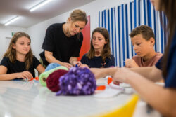 Four children listen attentively to the supervisor at a table full of colorful craft supplies.