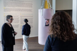 Een museumgids naast een roze bokszak geeft bezoekers informatie.
