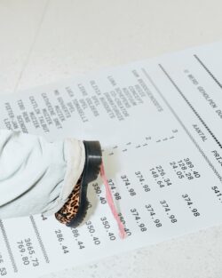 A person wearing light jeans and leopard print shoes stands on a large printed receipt with visible itemized prices and text.