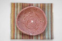 Coaster in roughly woven textile in a variety of colours with a handmade burgundy basket on it.
