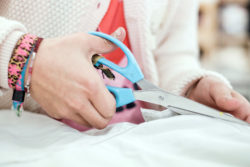 Een kinderhand met grote blauwe schaar knipt in een stuk textiel.