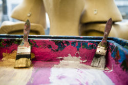 A variety of paint brushes in a wooden paint tray with pink paint in it.
