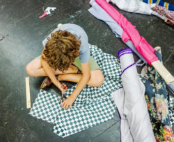A child sits on the floor and cuts into a large piece of black-and-white checkered textile.
