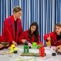 Four children in red craft clothes with paint stains are busy painting together with their supervisor.