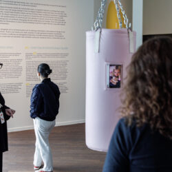 Een museumgids naast een roze bokszak geeft bezoekers informatie.