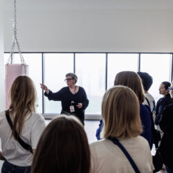 Een museumgids presenteert aan een publiek, waarbij ze met haar vinger een tentoongesteld stuk aanwijst en de betekenis ervan uitlegt.
