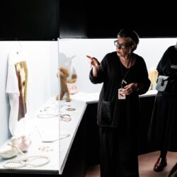 Een gids wijst naar een vitrine terwijl anderen de stukken in een museum bekijken.