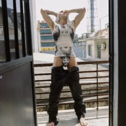 Een man in een broek met lage taille en een hemdje staat op een balkon, zijn hoofd in zijn handen en zijn ogen dicht, als belichaming van de Pride-campagne van Diesel.