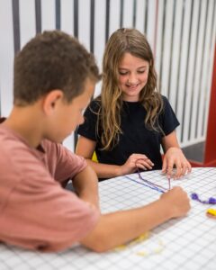 Twee kinderen zijn samen bezig met het maken van vriendschapsarmbandjes.