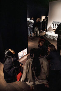 Jongeren verzameld op de grond in een exporuimte terwijl ze een kunstwerk bespreken.