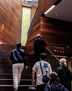 Een groep mensen die de trap opgaat in het atrium van een museum, omringd door grote ramen en moderne architectuur.