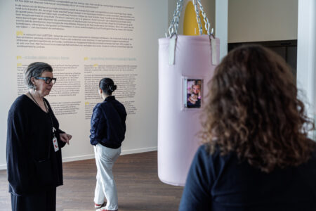 Een museumgids naast een roze bokszak geeft bezoekers informatie.