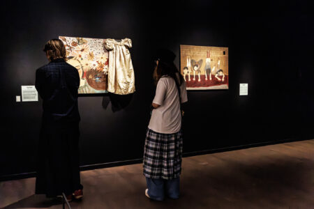 Two young people are looking at artworks in an exhibition space.