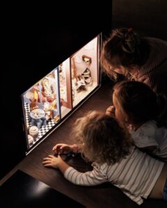 Three children are impressed by a diorama with mouse puppets and their interior.