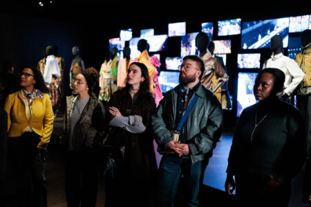 Young adults stand before a display of images at the Fashion Museum of Antwerp, showcasing Dries Van Noten's work.