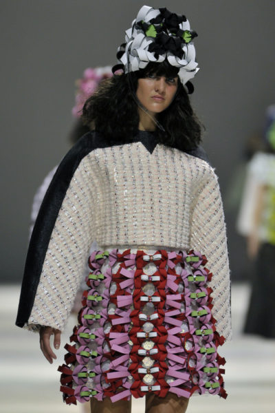 Catwalk model with a black-and-white headpiece, a white-and-silver top and a pink-and-green skirt