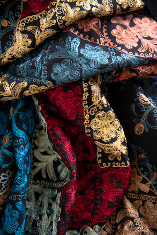 Detail van een stuk stof met geborduurde bloemen in verschillende kleuren.