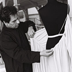 Een man, gekleed in het zwart, drapeert een witte jurk op een mannequin