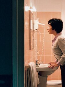 A woman looks at herself in a bathroom mirror.