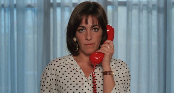 Een vrouw draagt een wit polkadot hemd en telefoneert met een rode telefoon