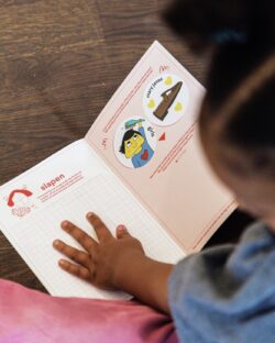 Een klein kind bladert in een opdrachtenboekje en legt het handje op een pagina.