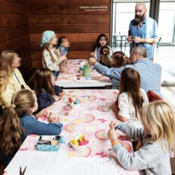 A group of parents and children are engaged in creative activities at a colorful table in the hall of a museum.