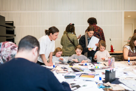 Een tafel met knutselmaterialen is omringd door ouders en kinderen die knutselen.