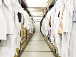 Image du dépôt des collections au MoMu, avec des gardes robes de chaque côté où les objets sont pendus ou rangés dans des sacs et des boites.