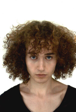 Passport photo of Floran Polano, he has curly brown hair and looks into the camera