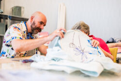 Een workshopbegeleider en een persoon met (ver)gevorderde dementie houden een borduurring vast