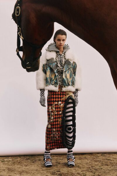 A model poses in a field in clothing designed by Annaëlle Reudink; a horse appears in view with its head