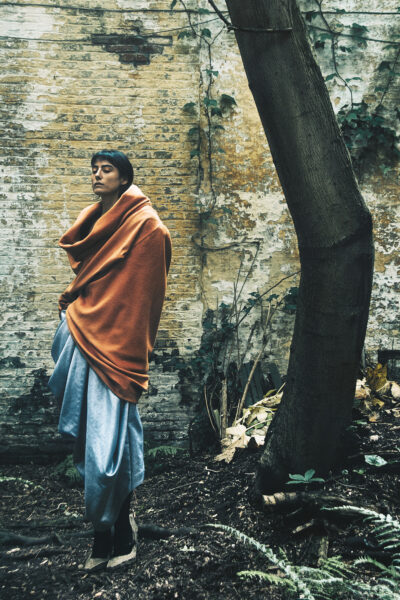 A model poses next to a tree in a city garden wearing clothes designed by Floran Polano