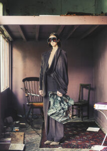 A model poses in a room with chairs, a music stand and books lying on a carpet