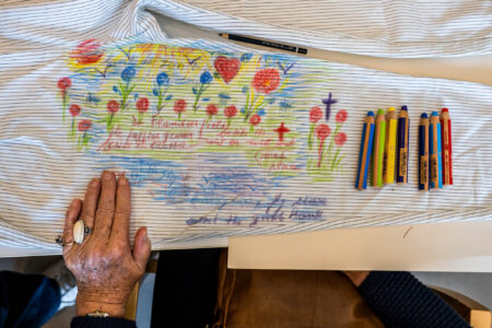 Een persoon met (ver)gevorderde dementie legt haar hand op een stuk textiel dat met behulp van kleurpotloden beschilderd is