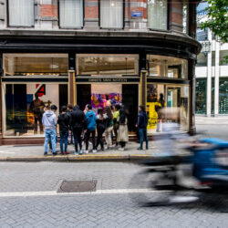 Groepje jonge mensen luistert naar een gids op de hoek van een straat, terwijl een fietser voorbij fietst.