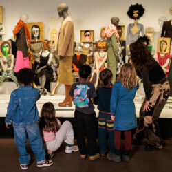 Kinderen verzamelen zich nieuwsgierig en geïnteresseerd rond een etalage met etalagepoppen die door Dirk Van Saene zijn gestyled.