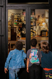 Drie kinderen gluren nieuwsgierig door een raam naar het atelier van Marina Yee tijdens de tentoonstelling over de Antwerp Six.
